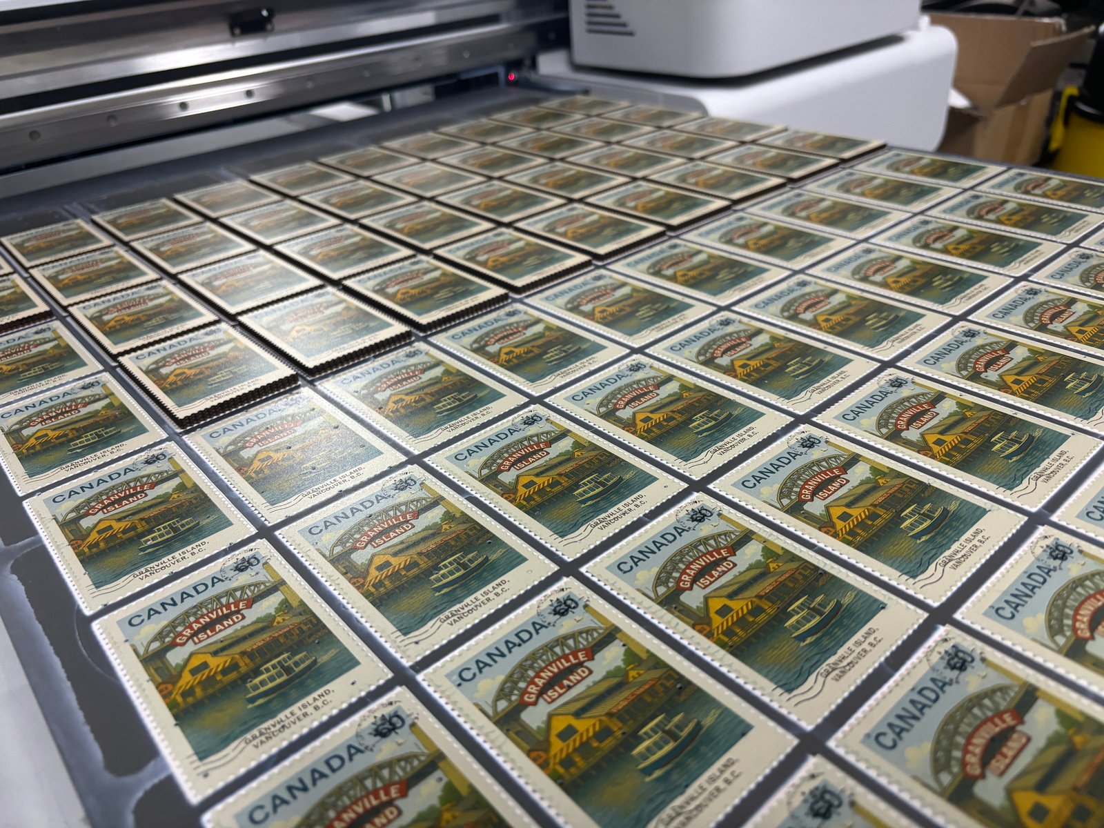 Custom stamp-style MDF souvenir fridge magnets on UV printing machine showing production scale