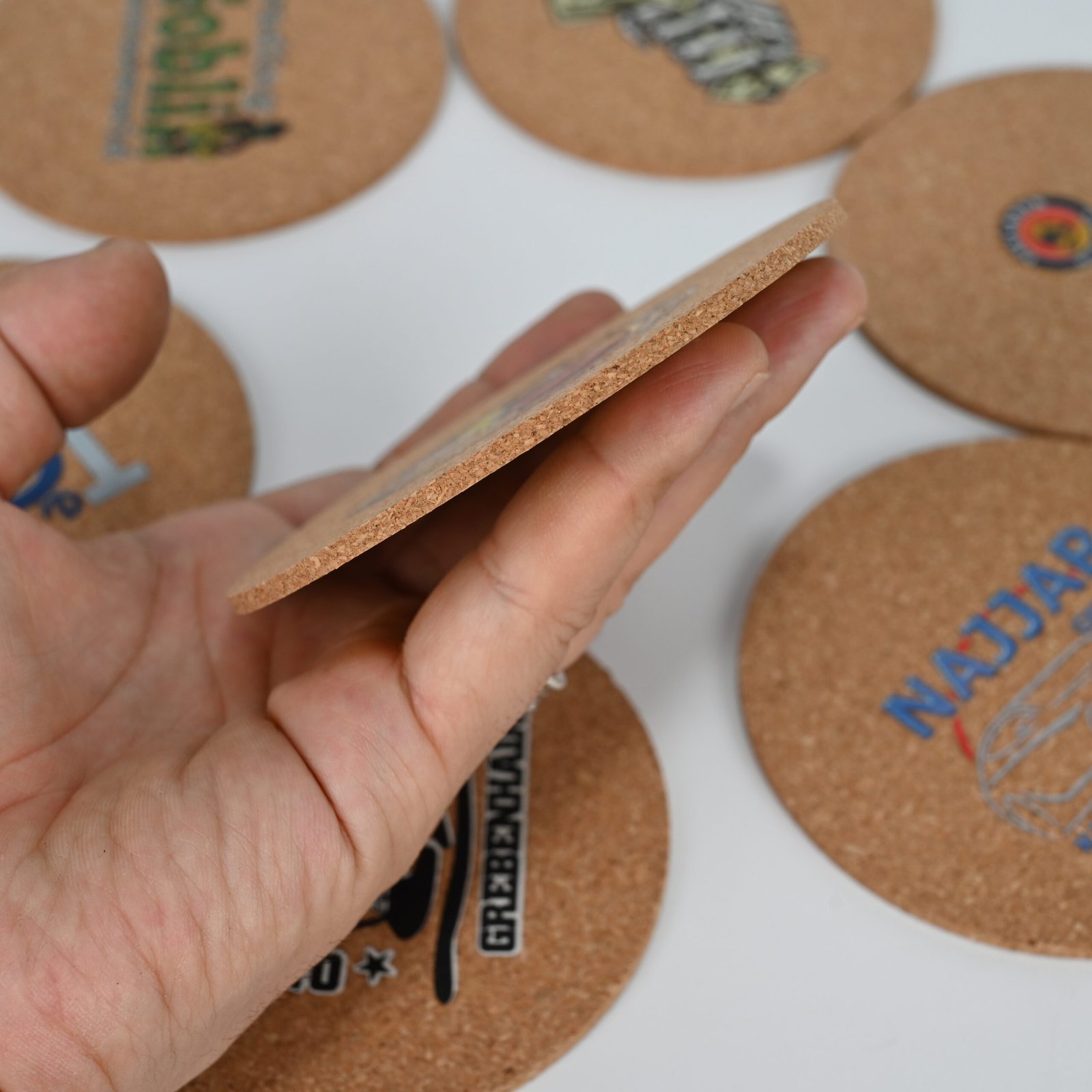 Hand holding round cork coaster sideways showing thin profile and edge quality